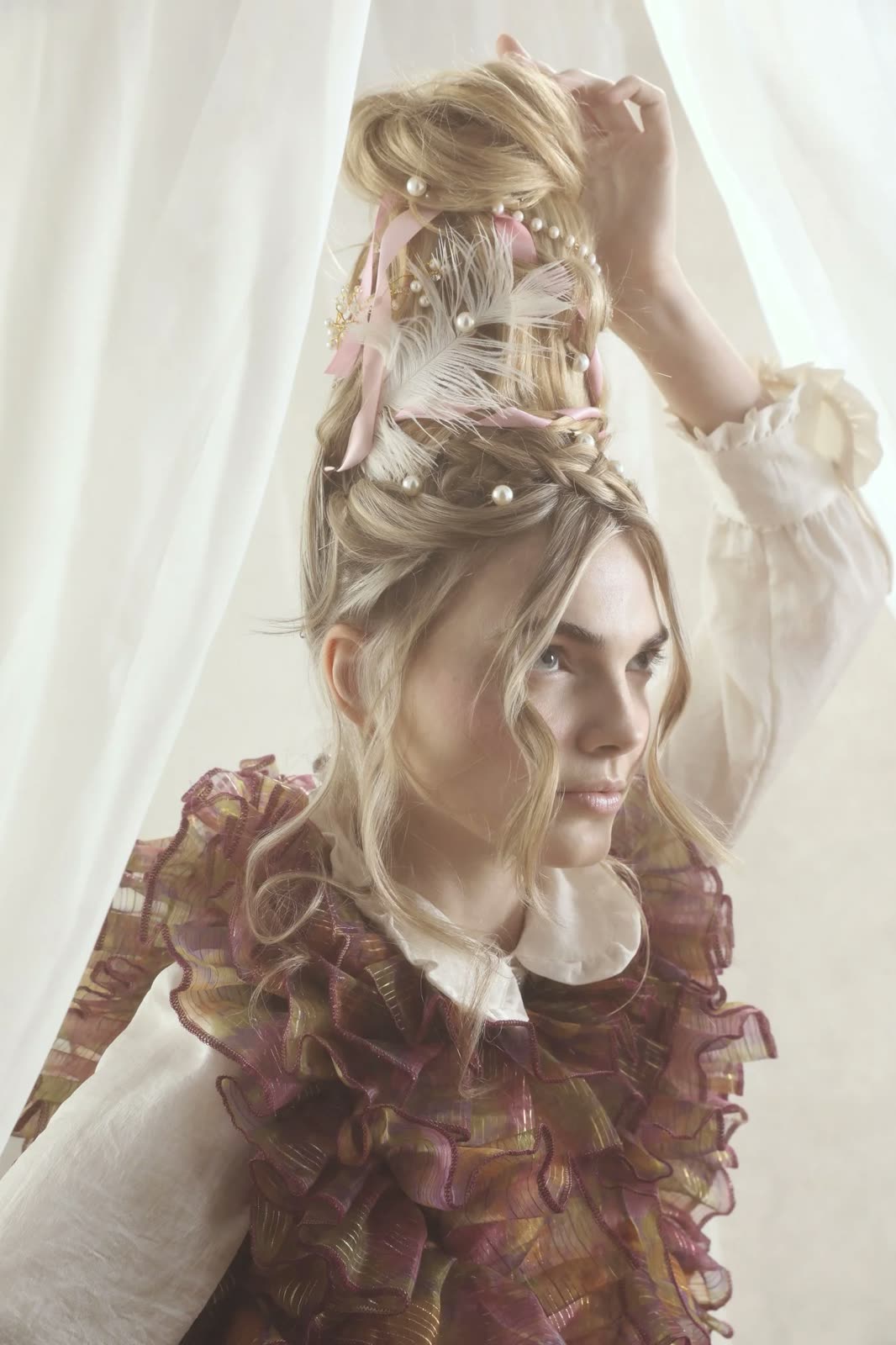 Woman with a tall updo trimmed with pearls, ribbons and feathers, in a ruffled plum organza top
