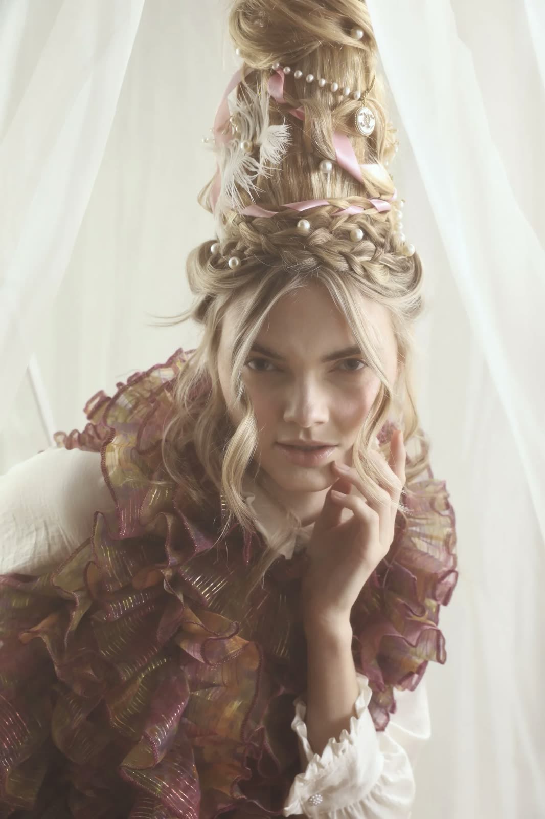 Close-up of a woman with a pearl and ribbon updo and a ruffled plum and gold collar