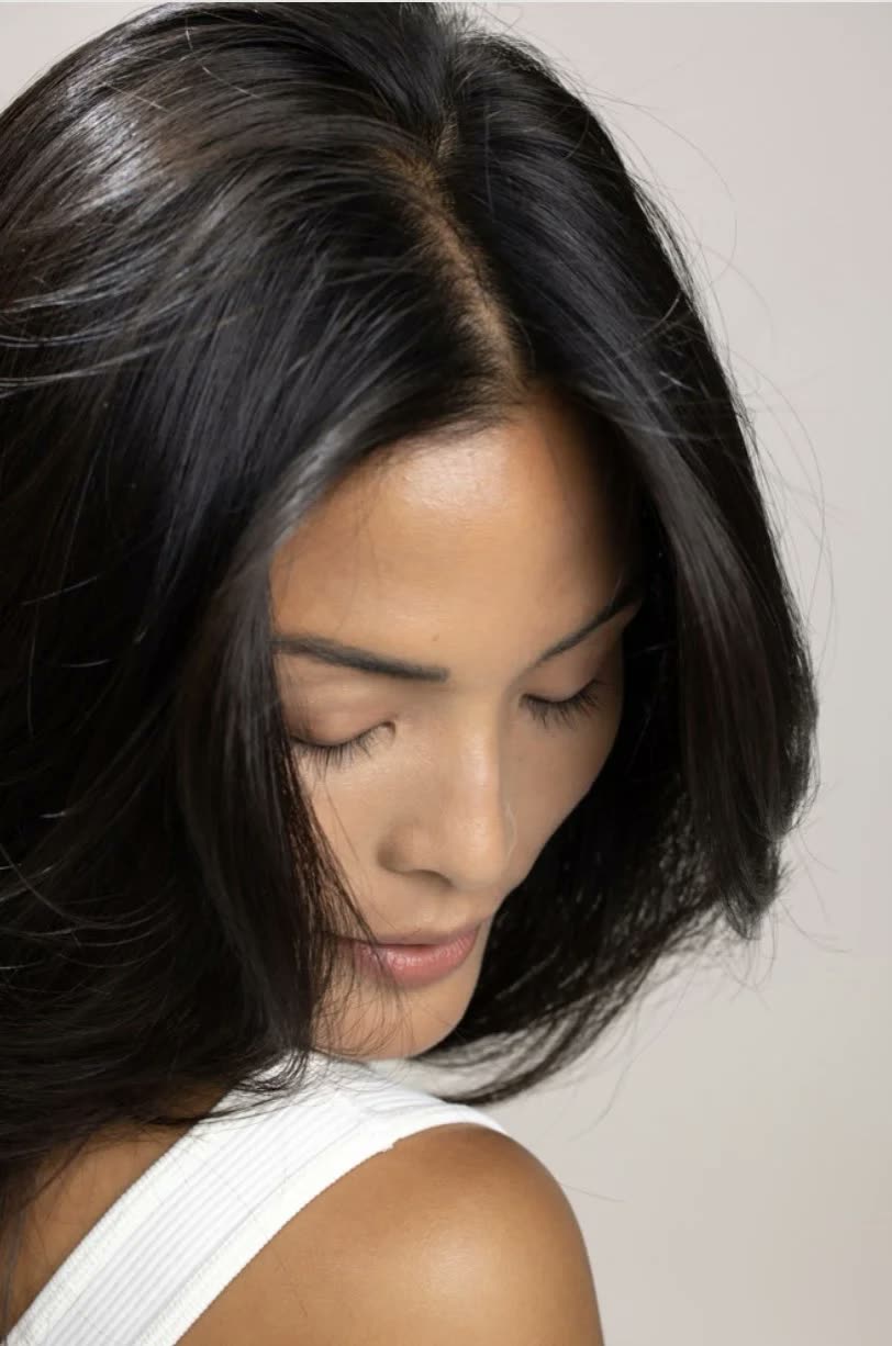 Woman with a glossy black shoulder-length cut looks down, in a white tank top