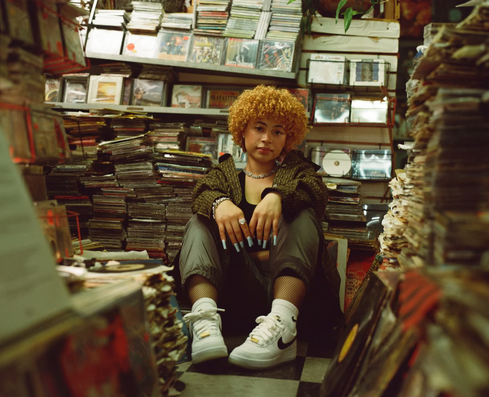Ice Spice sits among stacks of records and CDs in white Air Force 1s