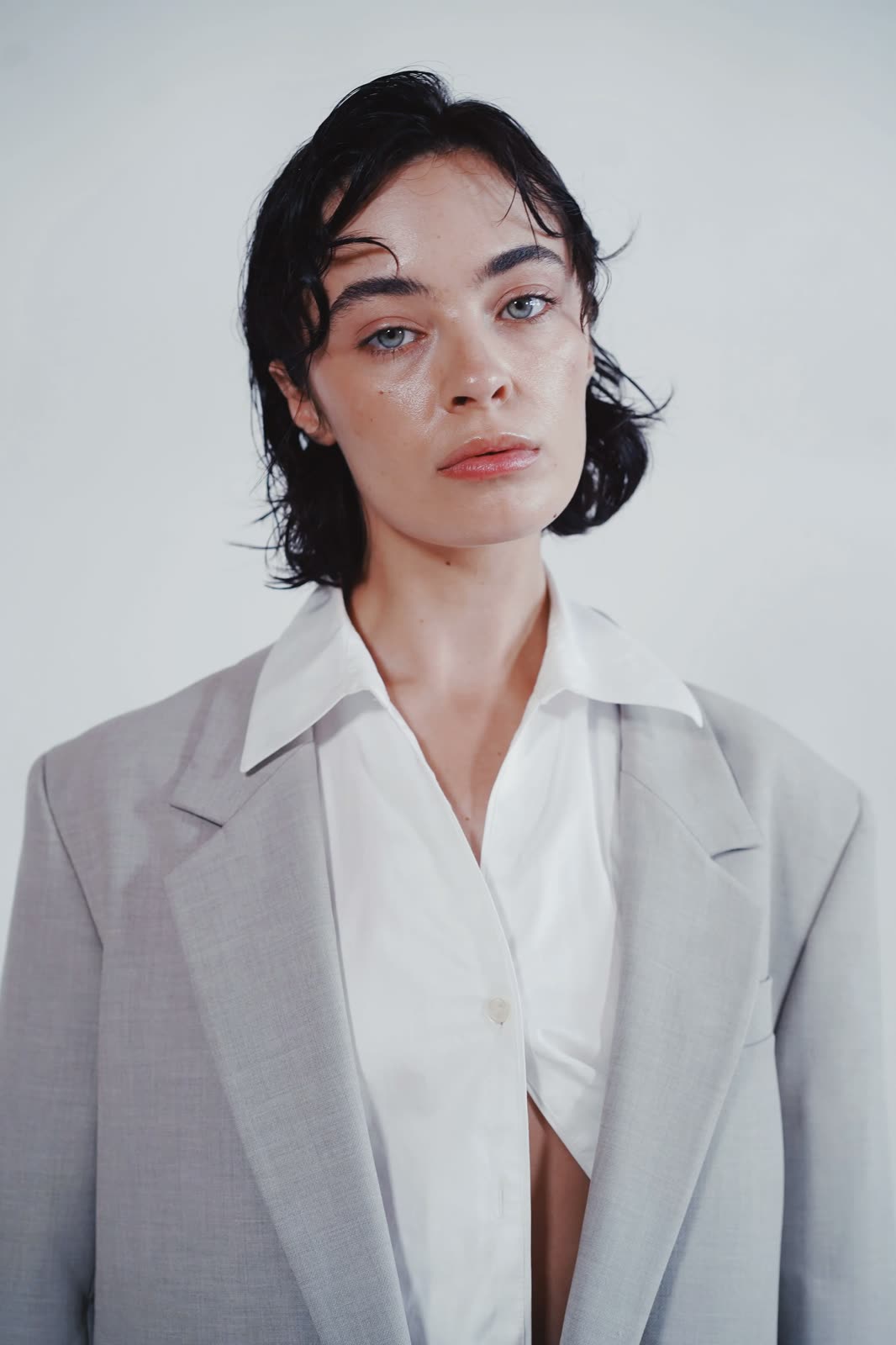 Reilly Hail with slicked dark hair in a grey blazer over an open white shirt