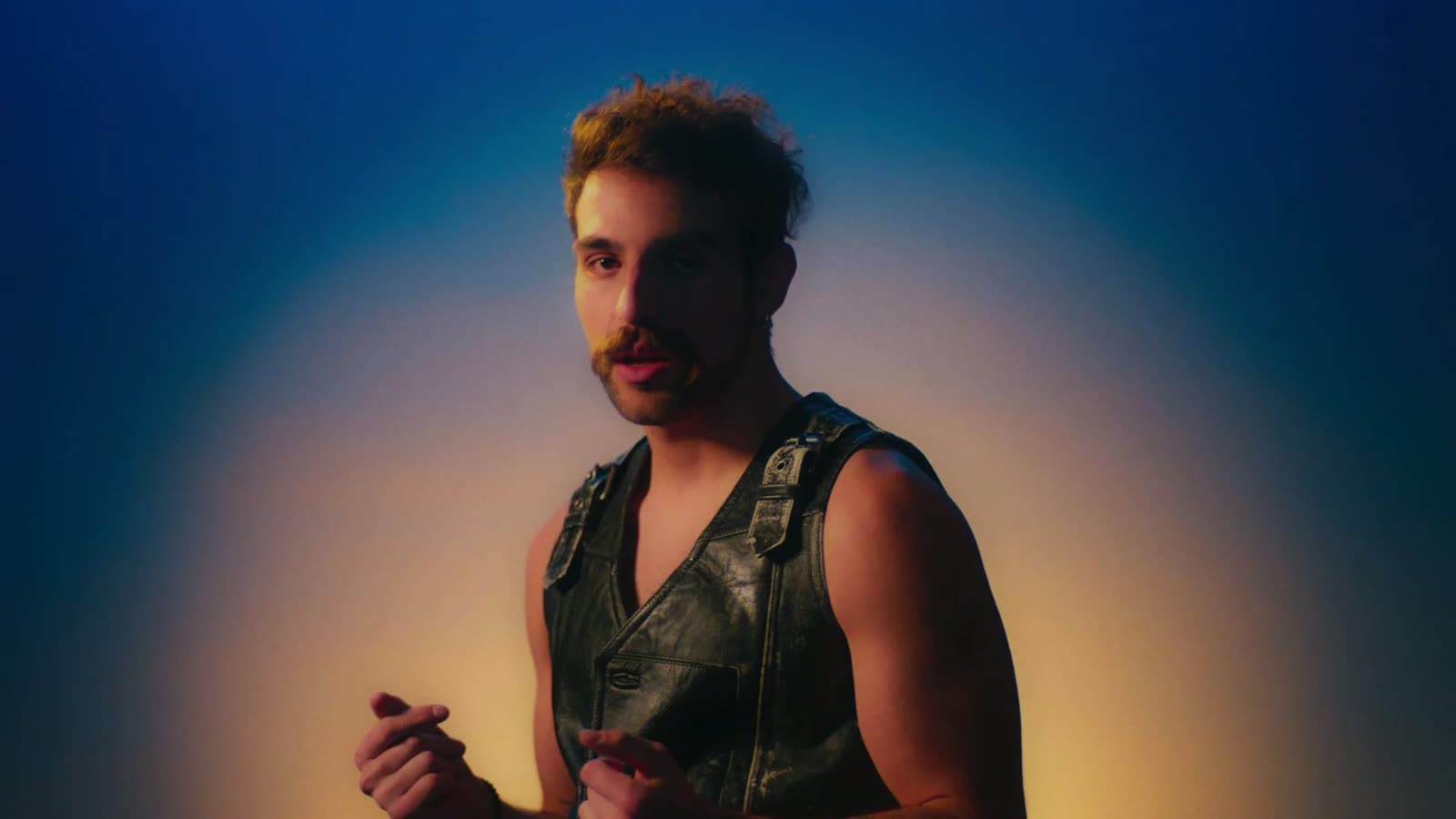 Man in a black leather vest against a blue and orange gradient, Facetime video still