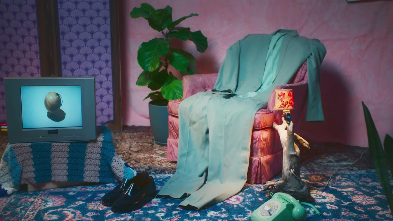 Sage suit draped over a pink armchair beside an old TV and a green phone, Facetime video still